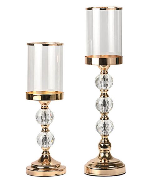 Ένα εντυπωσιακό σετ κηροπηγίων που εστιάζει στην έντονη λάμψη των κρυστάλλων. Σχεδιασμός: Χρυσή βάση και κορμός με πολυεδρικές (faceted) κρυστάλλινες μπάλες που θυμίζουν διαμάντια και διαθλούν το φως. Λεπτομέρεια: Το κυλινδρικό γυαλί διαθέτει χρυσό τελείωμα στο επάνω μέρος, προσδίδοντας ακόμα μεγαλύτερη πολυτέλεια.